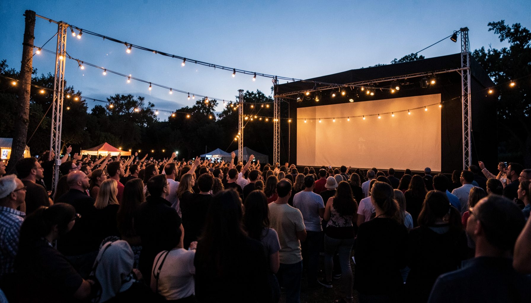Outdoor film festival screening at dusk with string lights and a large projection screen, warm amber and navy blue evening tones